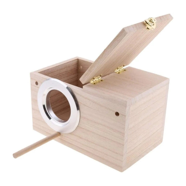 A light natural wood birdhouse with an open hinged lid, a silver metal perch, and a wooden stick on a white background.